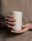 Tall Column mug in sand held in hand, handmade stoneware with glazed interior and unglazed exterior, Archive Studio